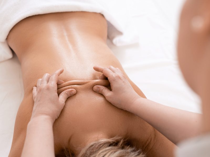 Over shoulder view of masseur performing deep tissue massage of womens back to release pain